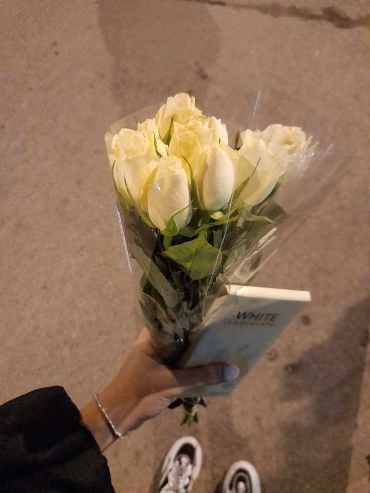 a person holding a bouquet of white roses and an open book in their hand while standing on the sidewalk