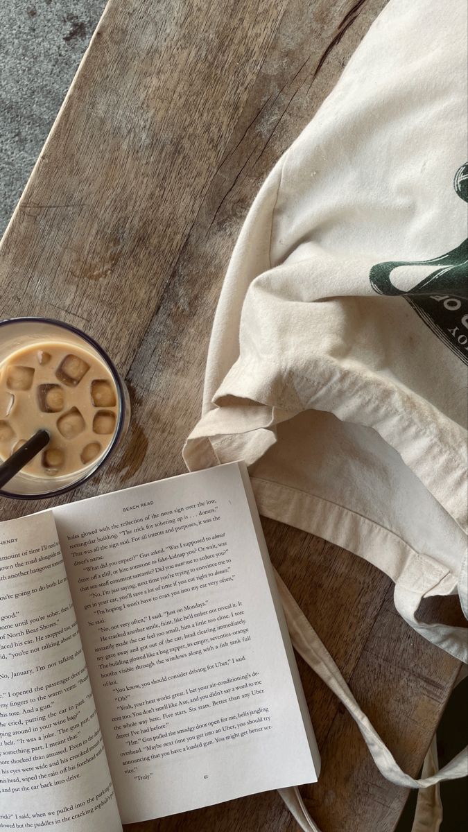 an open book sitting on top of a wooden table next to a cup of coffee