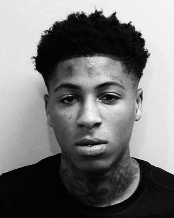 a black and white photo of a young man with tattoos on his face looking at the camera