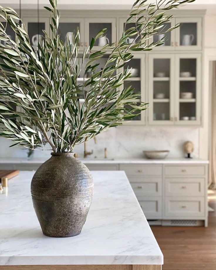 a vase filled with green plants on top of a white marble countertop in a kitchen