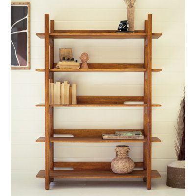 a wooden shelf with books and vases on it in front of a white wall