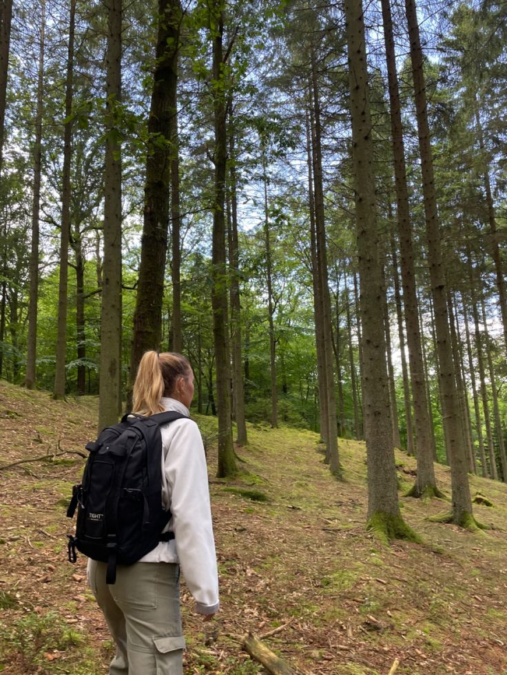 a woman is walking through the woods with her back to the camera and looking up at the trees