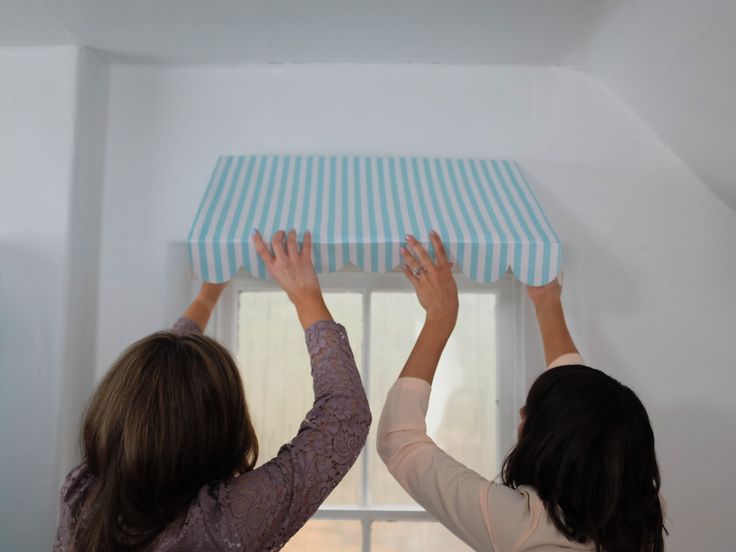 two women holding up a blue and white striped awning over a window sill