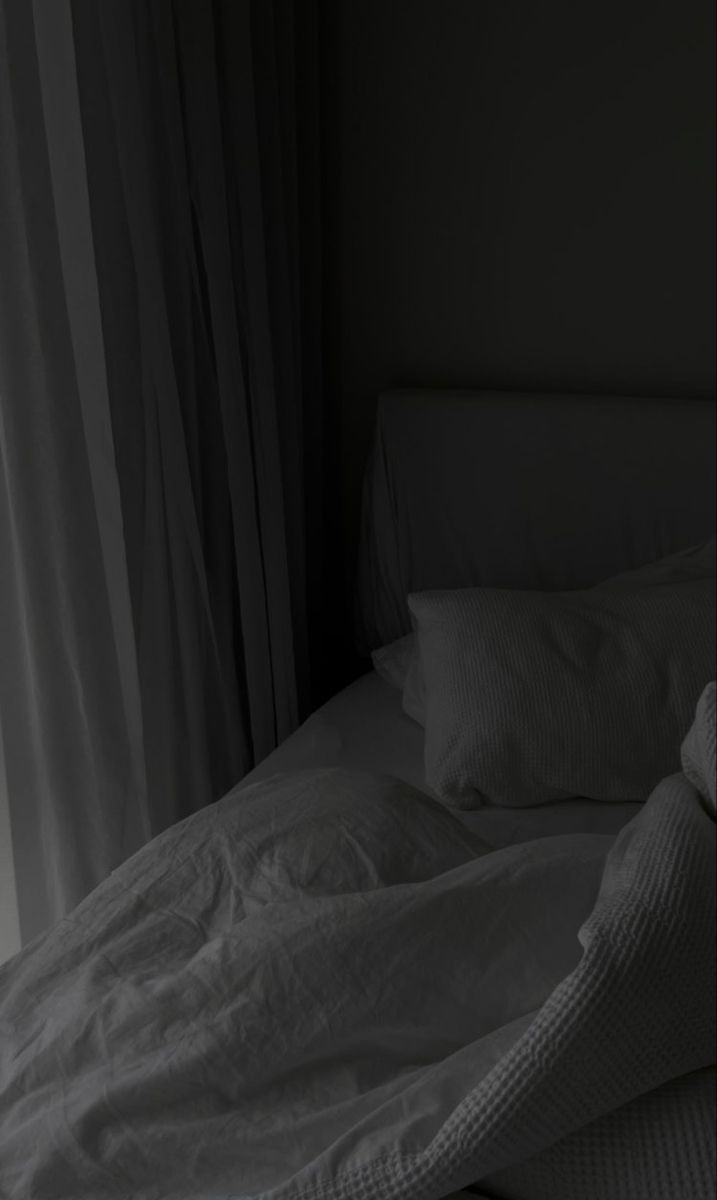 an unmade bed in a dark room with white sheets and pillows on top of it