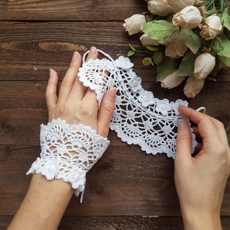 two hands holding white lace on top of a wooden table next to flowers and a vase