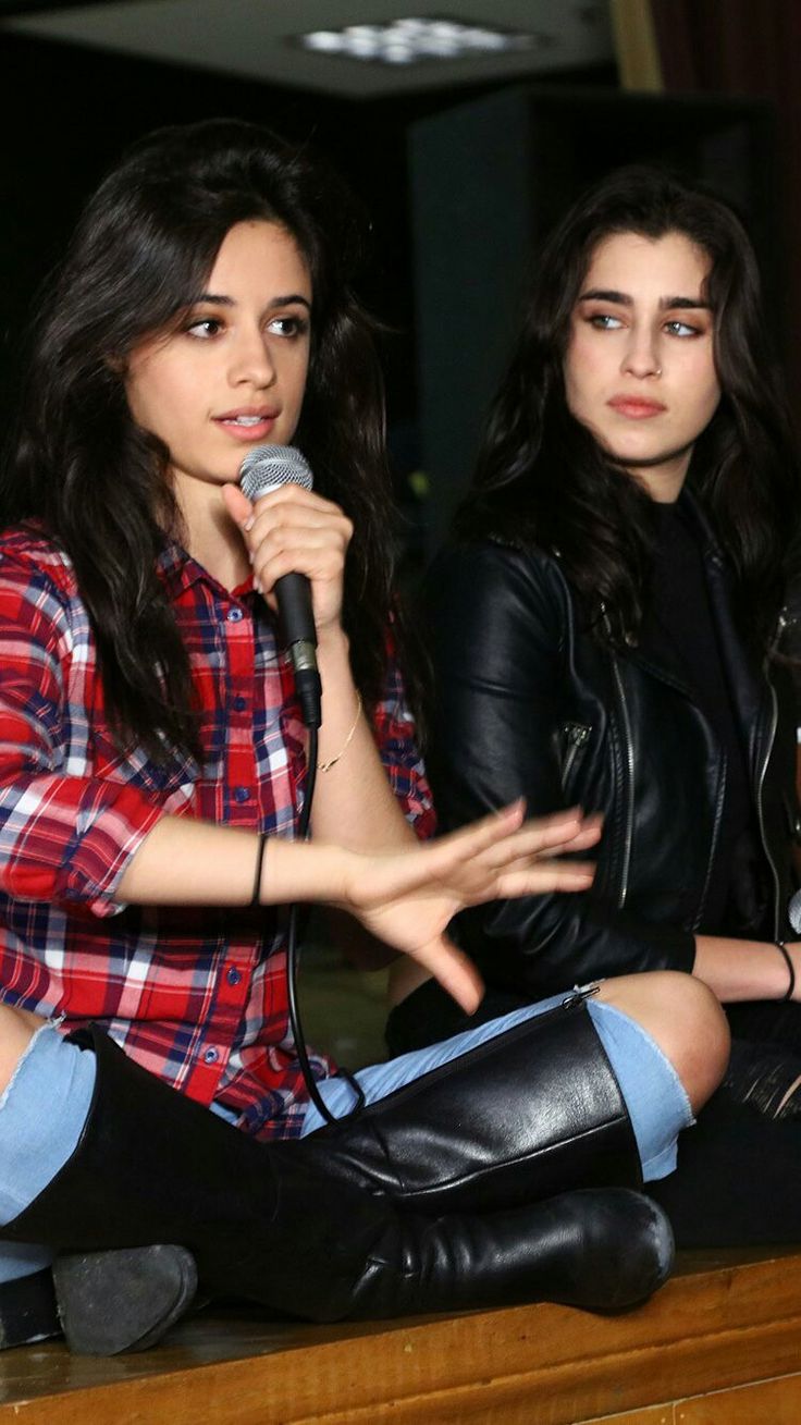 two young women sitting on top of a wooden table with microphones in their hands