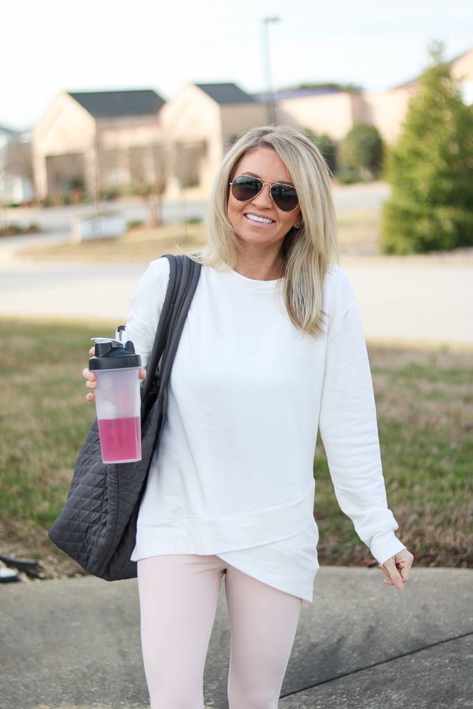 a woman in white shirt and pink leggings holding a coffee cup while walking down the street