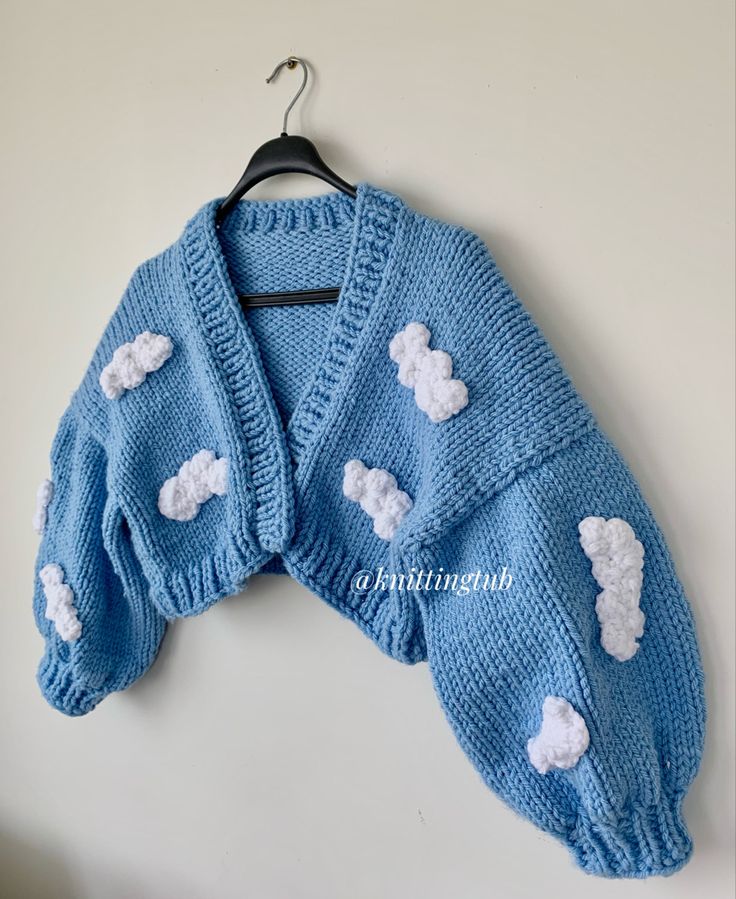 a blue knitted sweater with white clouds on the back, hanging from a hanger