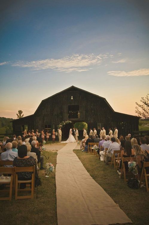 a bride and groom walking down the aisle to their wedding ceremony in front of an old barn