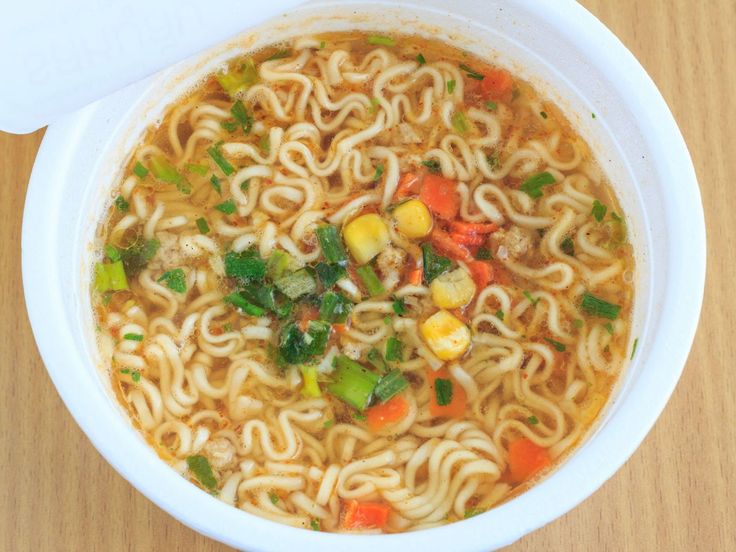 a bowl of soup with noodles, carrots and other vegetables in it on a wooden table