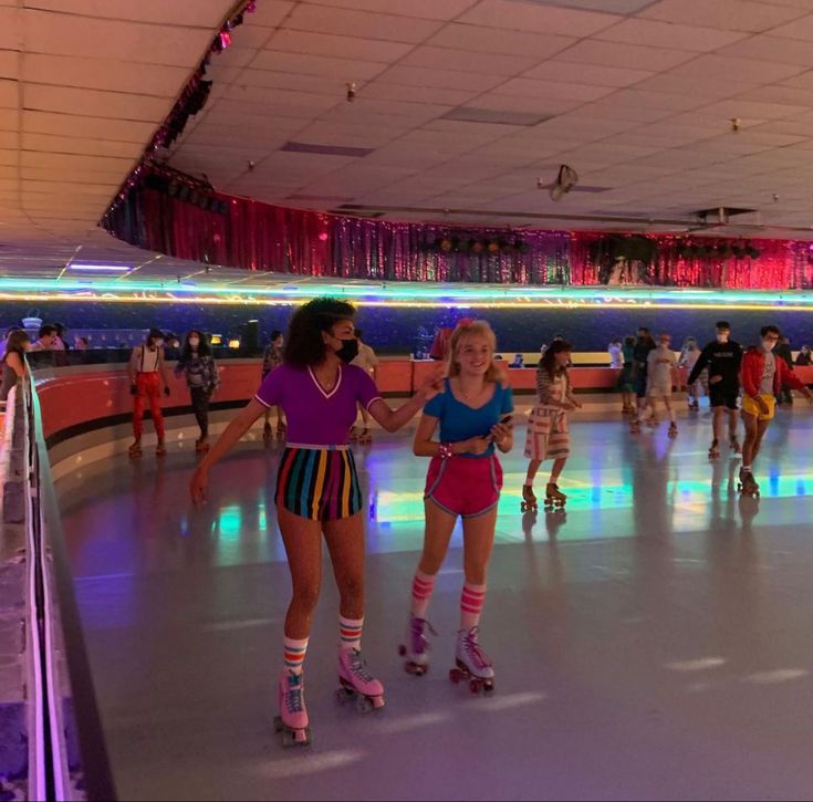 two girls on roller skates in an indoor skating rink with lights and people walking around