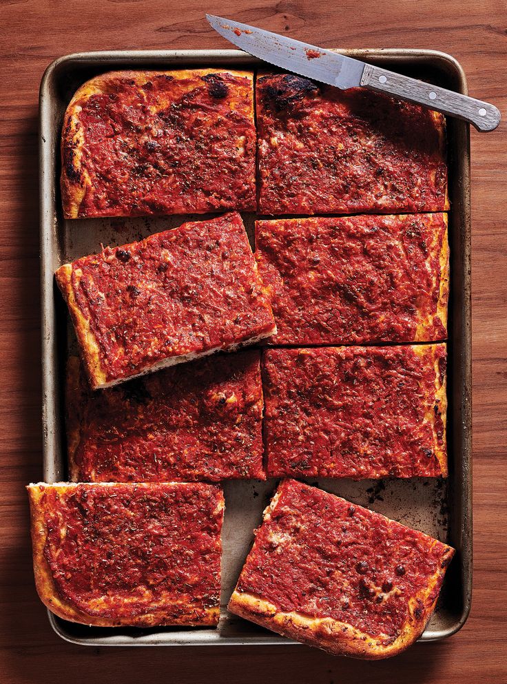 square slices of deep dish pizza in a pan with a spatula on the side