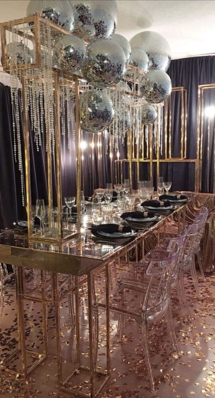 a long table is set with black plates and silver balloons