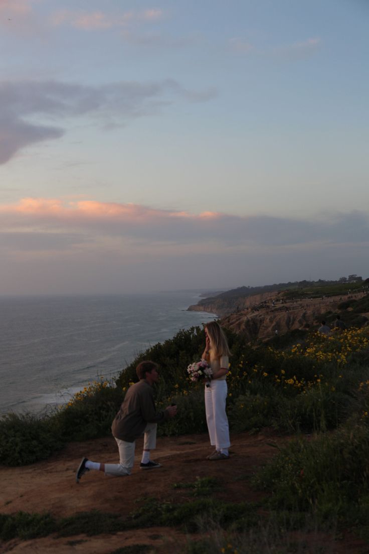 two people standing on top of a hill next to the ocean