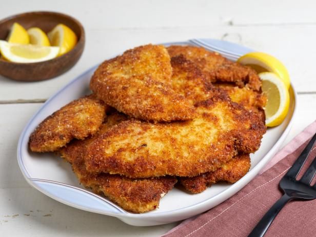 some fried food on a white plate with lemon wedges and a fork next to it