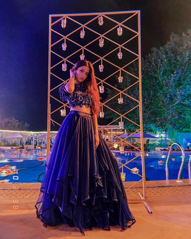 a woman standing in front of a pool wearing a blue and black dress with long sleeves