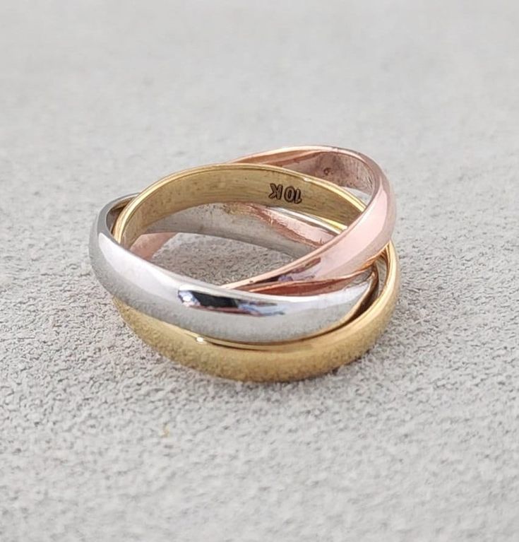 three different colored gold and silver wedding rings on the ground with white sand in the background