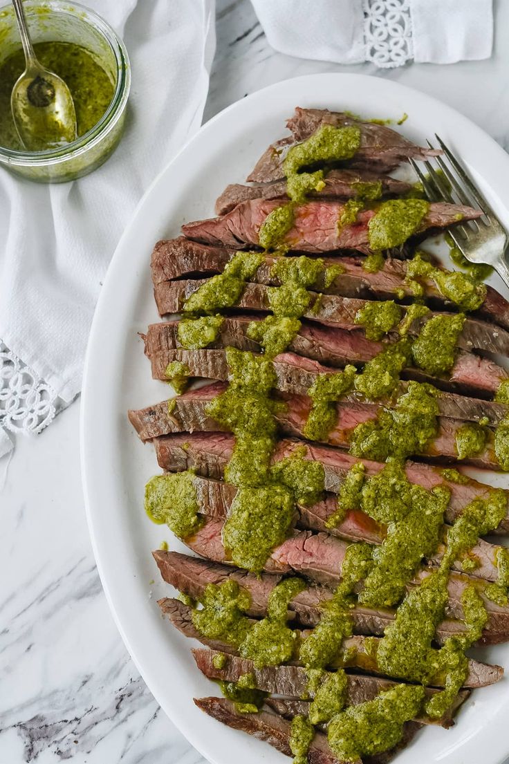 a white plate topped with steak covered in green sauce and garnished with pesto