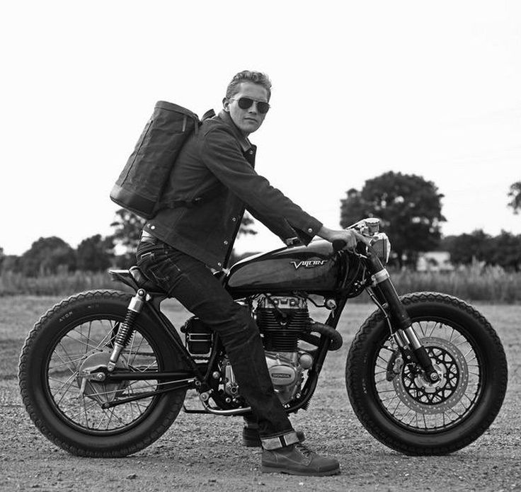 a man sitting on top of a motorcycle with a bag strapped to the back of it