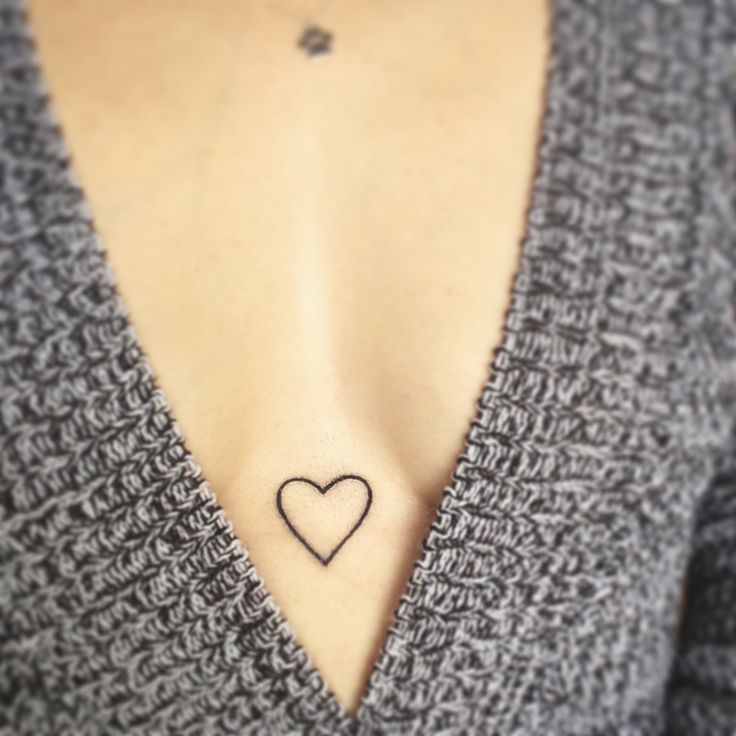 a woman's chest with a small heart tattoo on the left side of her chest