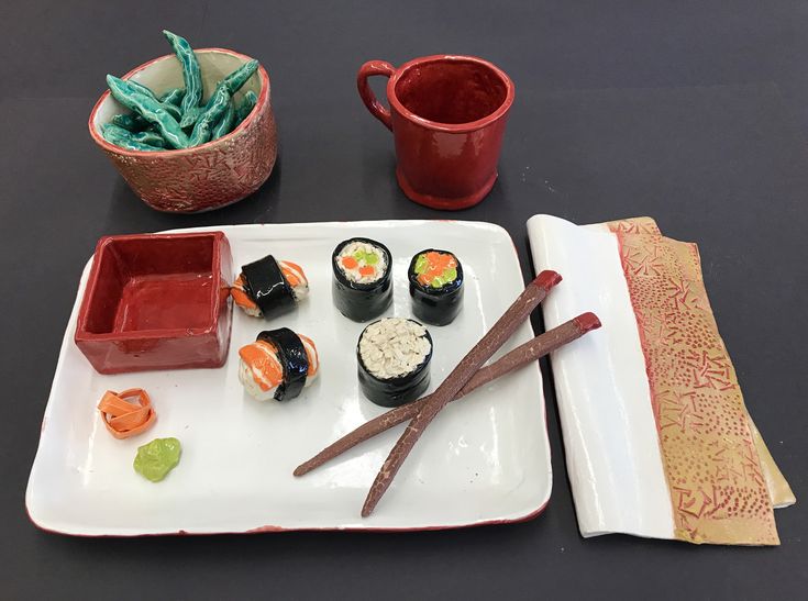 sushi and chopsticks sit on a plate next to two red mugs