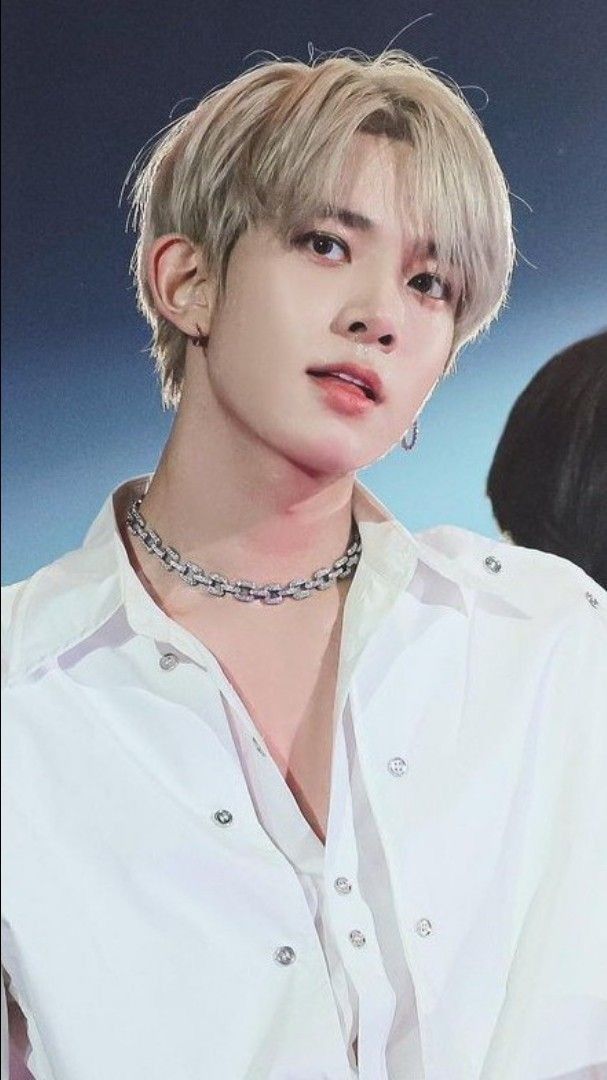 a man with blonde hair wearing a white shirt and silver choker on his neck