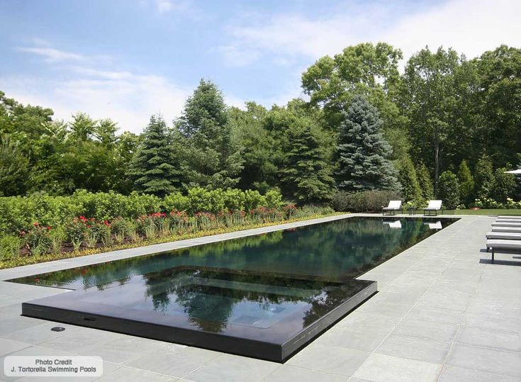 an empty pool surrounded by lounge chairs in the middle of a garden with lots of trees