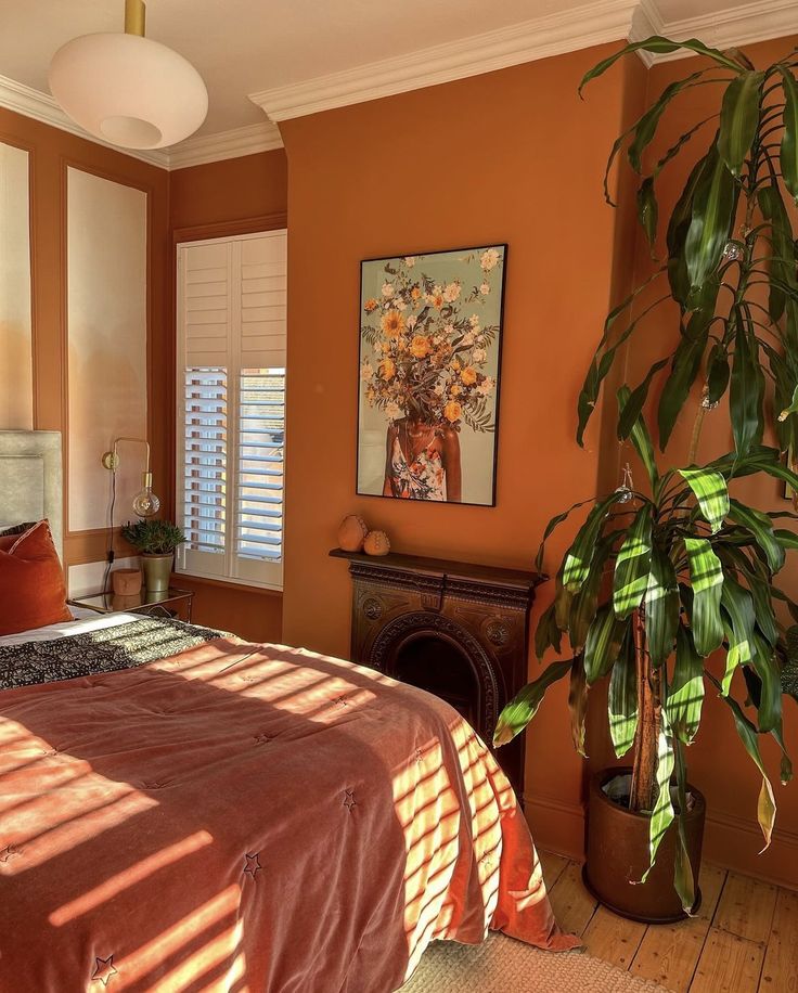 a bedroom with an orange wall and wooden flooring has a plant in the corner