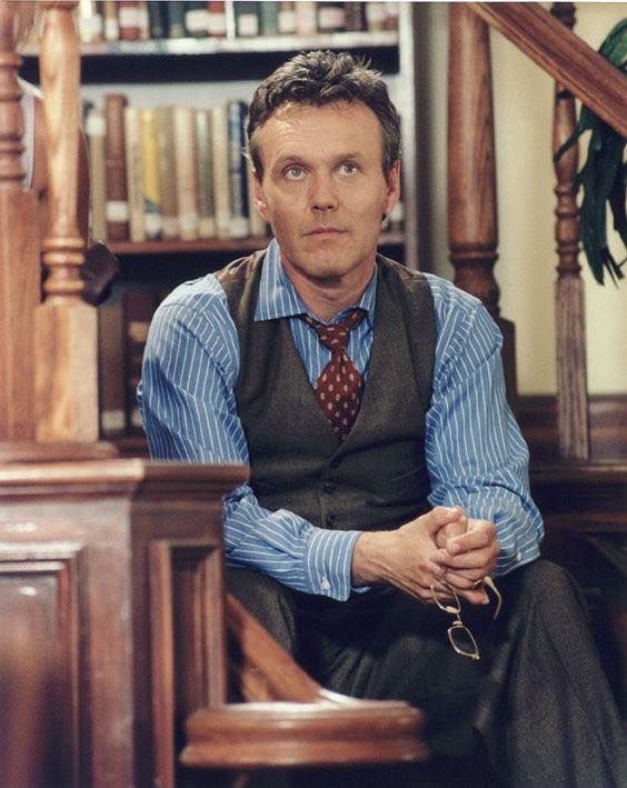 a man sitting on top of a wooden chair in front of a bookshelf