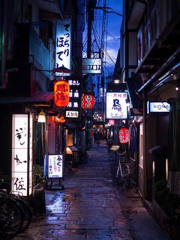 an alley way with signs and bicycles parked on the side walk at night in japan