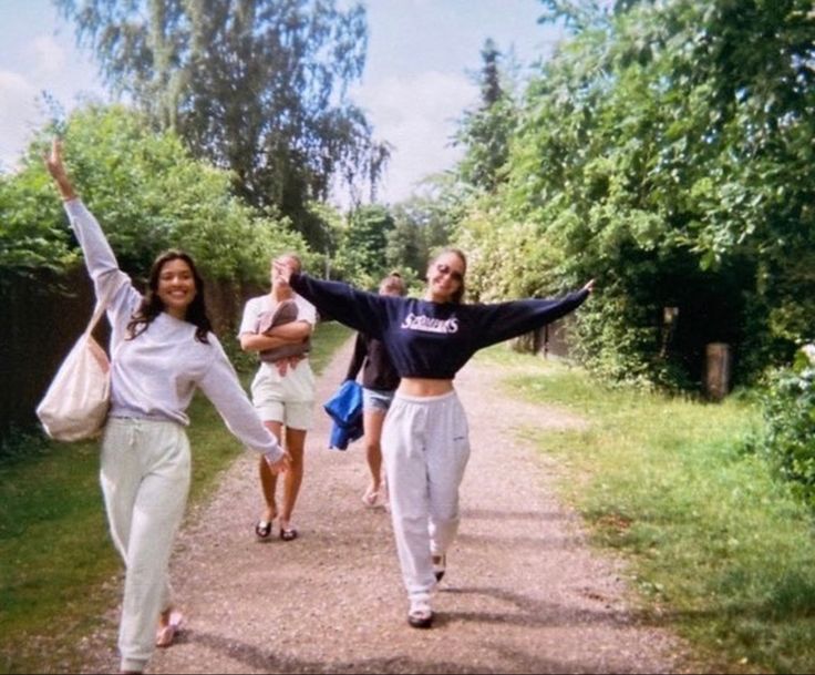 two women walking down a dirt road with their arms in the air and one holding her hands up