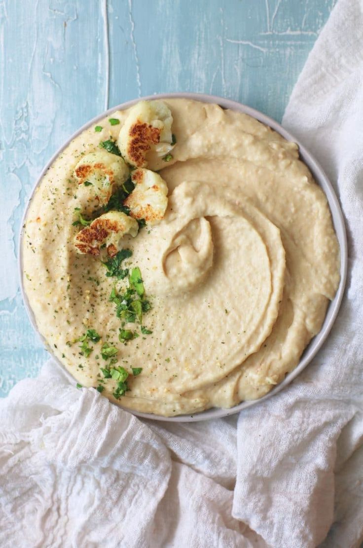 a bowl filled with hummus and scallops on top of a white cloth