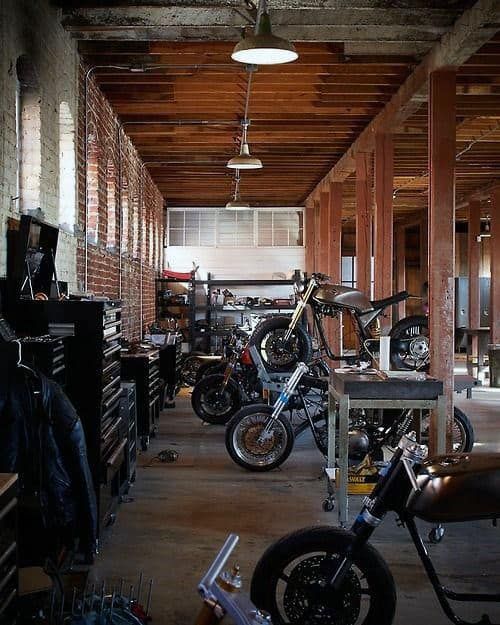 several motorcycles are parked in a garage with brick walls and beams on either side of the room