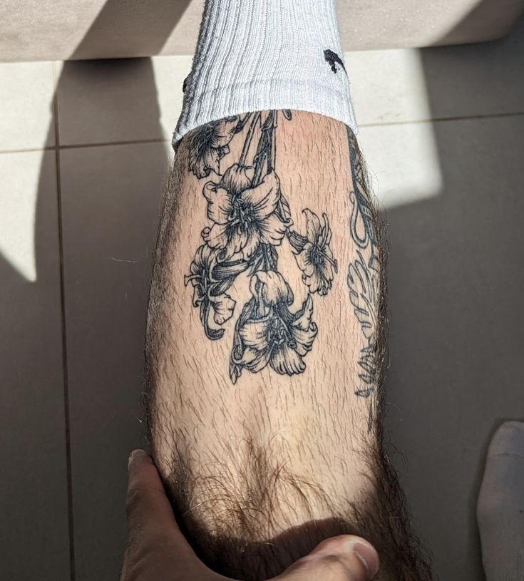 a man's arm with flowers on it and a white shirt underneath his leg