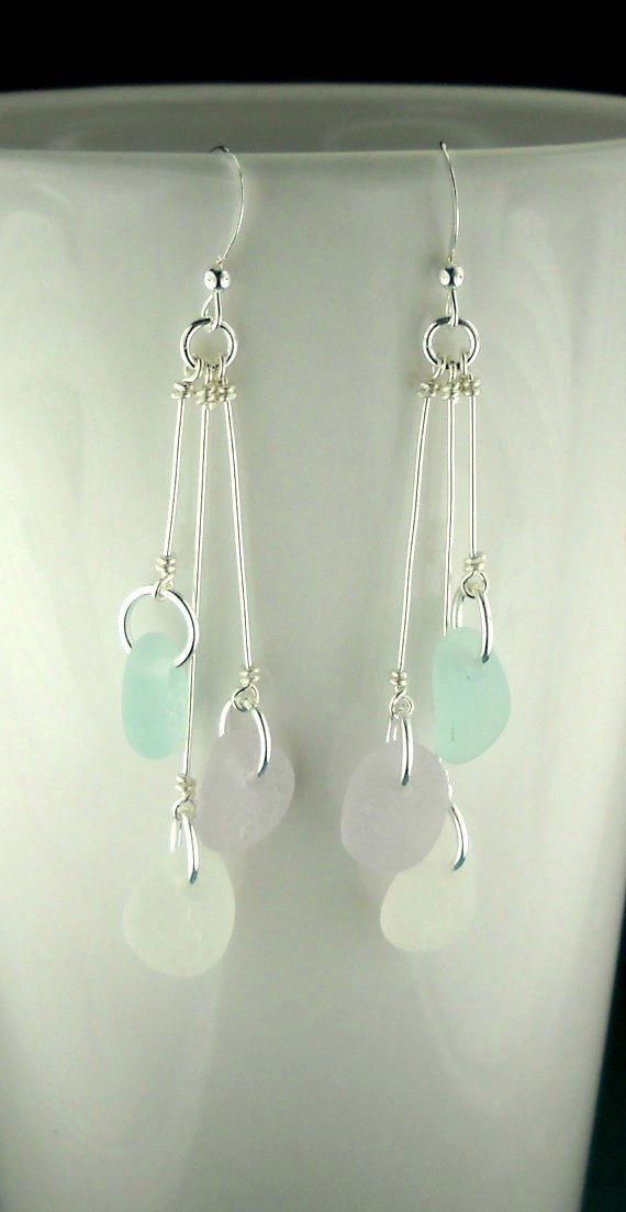 a pair of white and green glass earrings on a stand with a black surface in the background