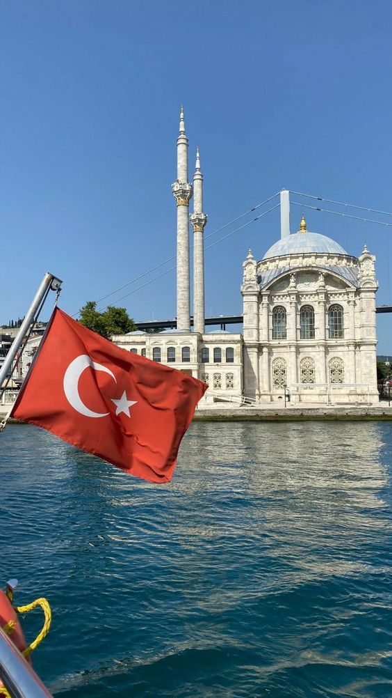 a turkish flag flying in front of a building on the side of a body of water