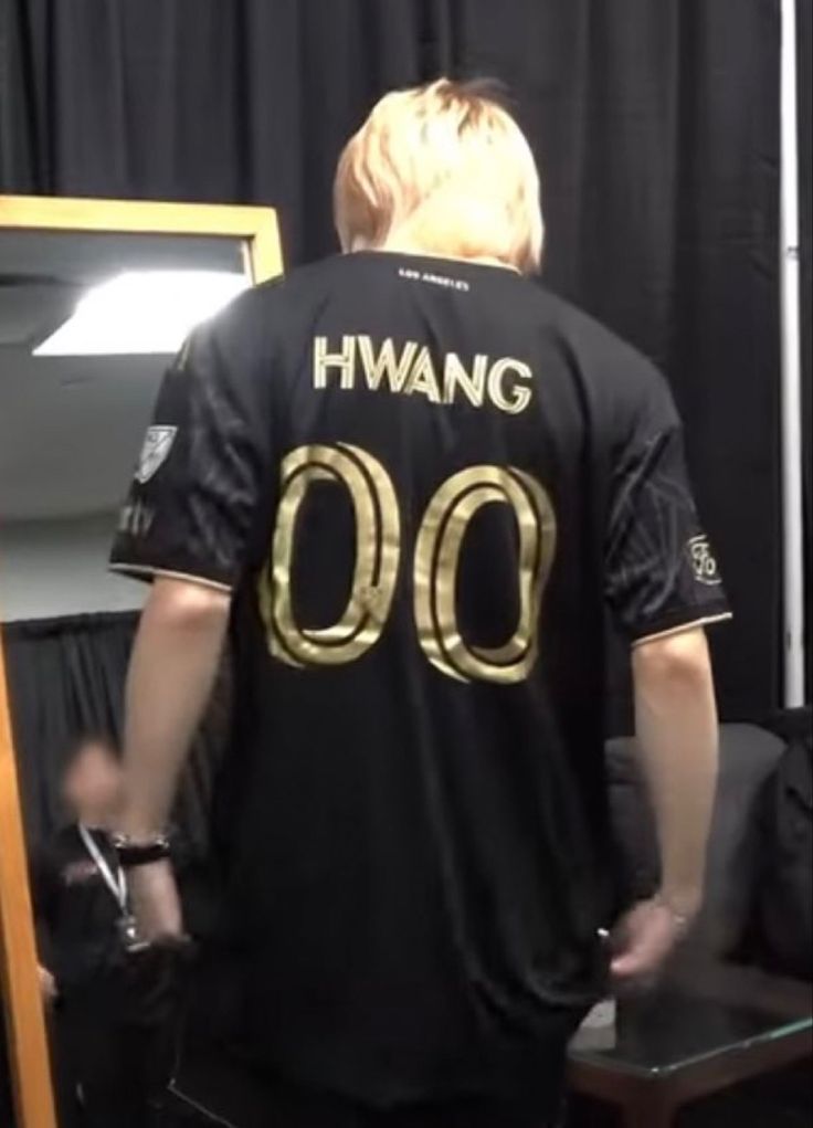 a man standing in front of a mirror wearing a black shirt with gold lettering on it