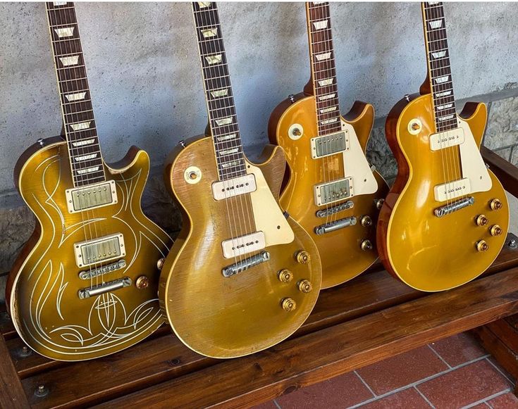 three guitars are lined up on a shelf in front of a brick wall, one is yellow and the other is brown