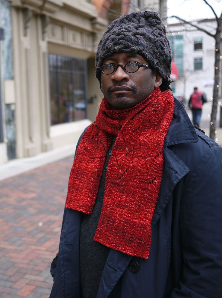 a man wearing a red knitted scarf and hat standing in front of a building