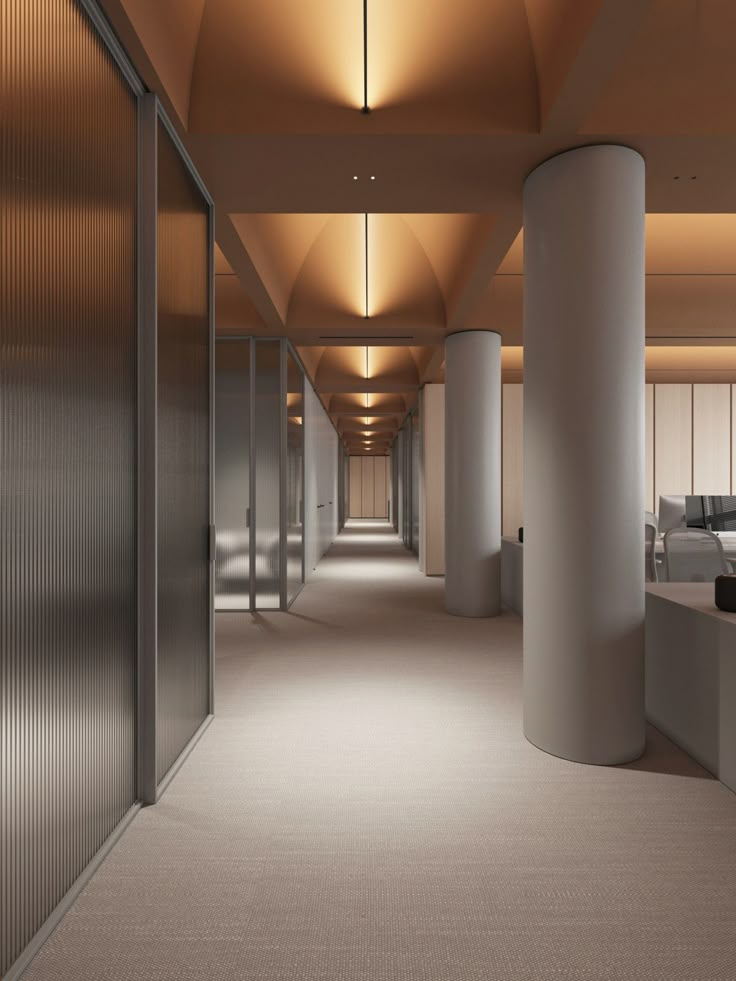 an empty office hallway with columns and lights on either side of the corridor is lit by recessed lighting