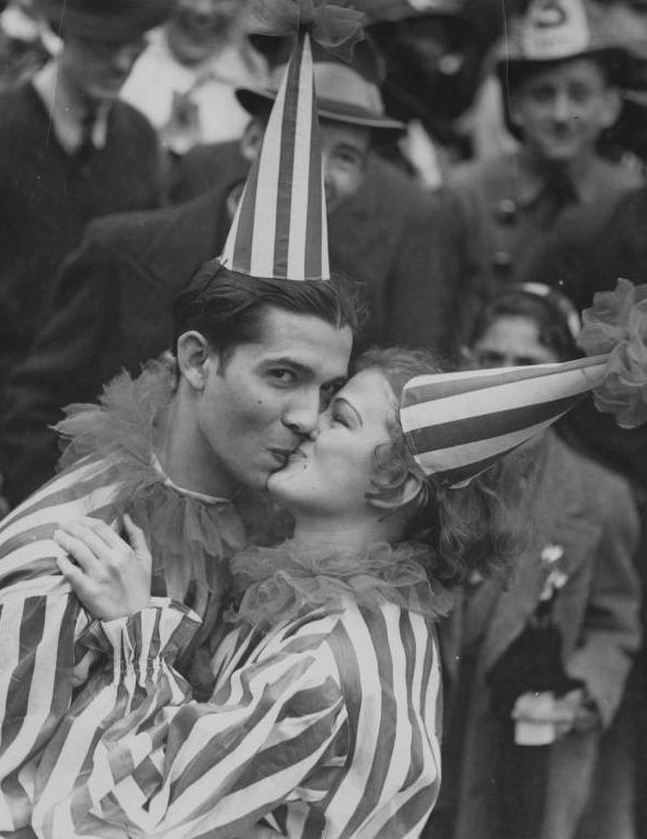 a man kissing a woman wearing a clown hat while standing in front of a crowd