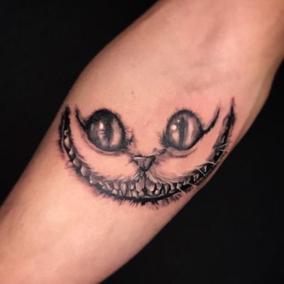 a black and white cat tattoo on the left arm, with eyes drawn to look like it's smiling