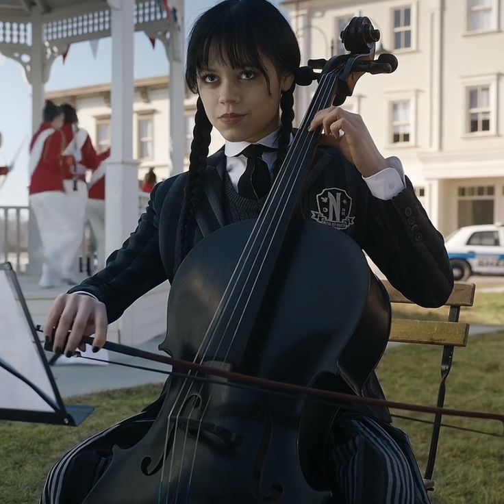 a woman with long hair holding a cello in front of a building and playing music