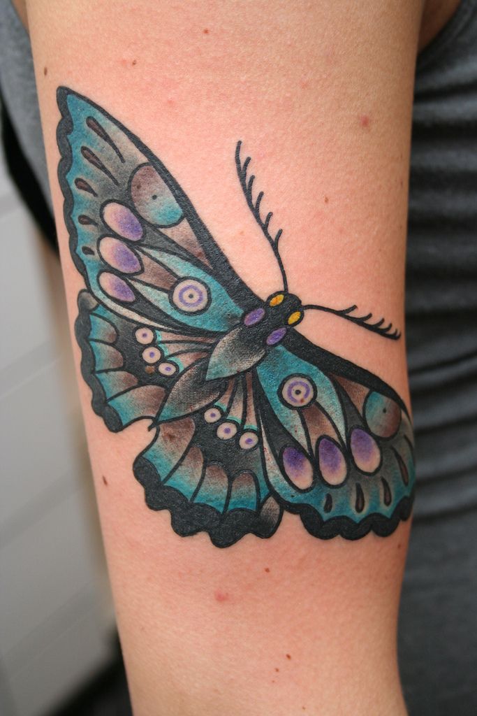 a woman's arm with a blue and black butterfly tattoo on the left shoulder