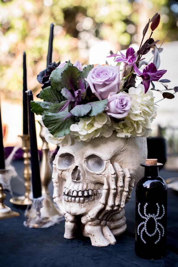 a skull vase with flowers in it sitting on a table next to candles and bottles