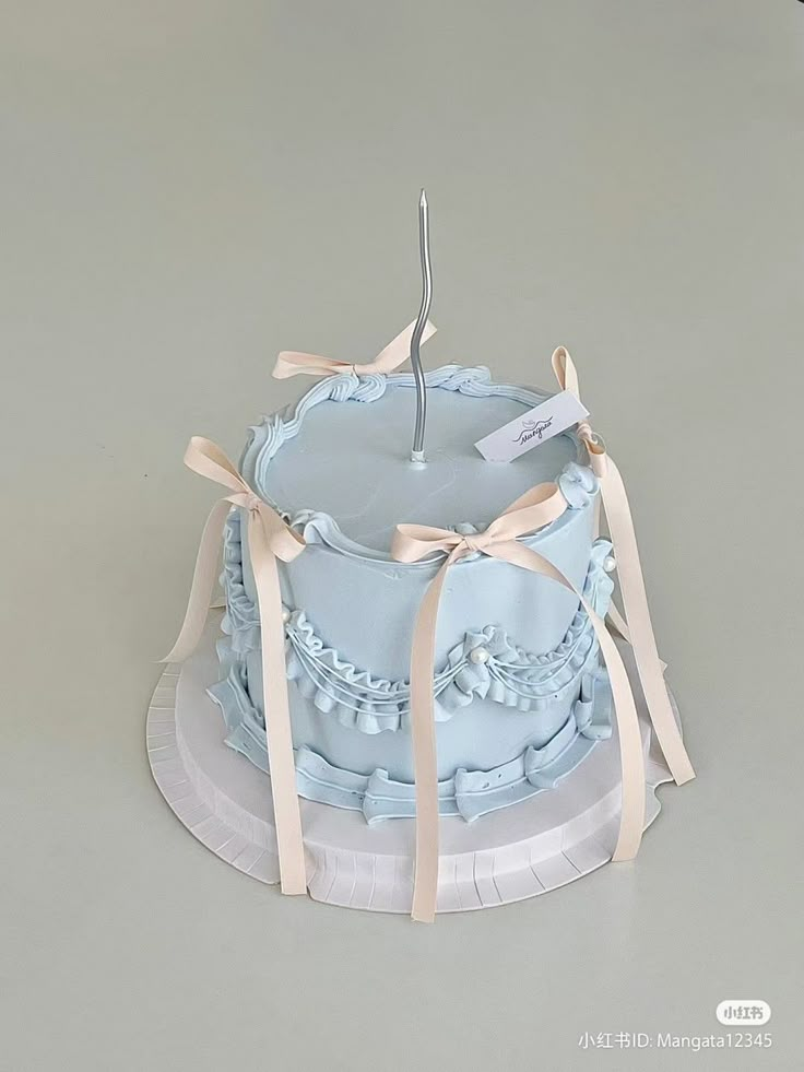 a blue cake sitting on top of a white plate covered in ribbon and a single candle