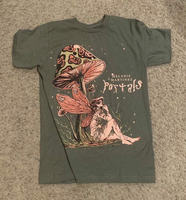 a green t - shirt with an image of a fairy sitting on the ground next to a mushroom