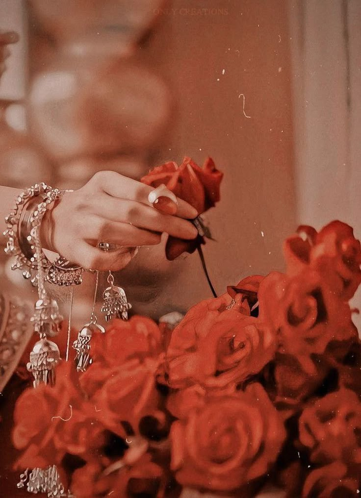 a woman is holding a rose in her hand and looking down at the roses that are being held by her hands