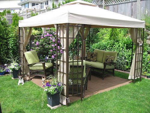 a gazebo sitting in the middle of a lush green yard with lots of flowers