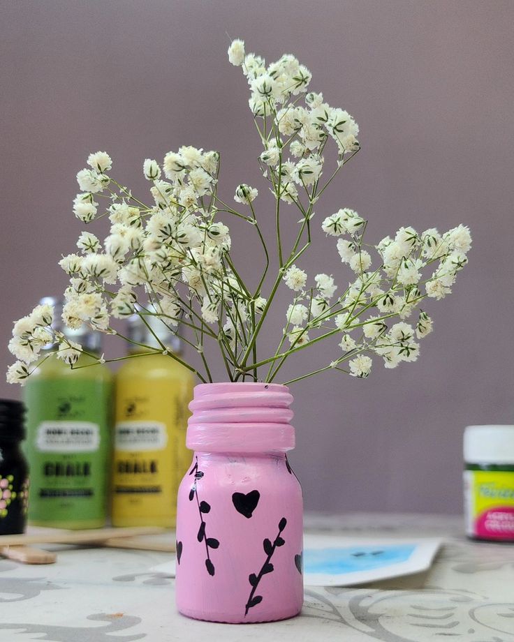 a pink mason jar with white flowers in it on a table next to other jars